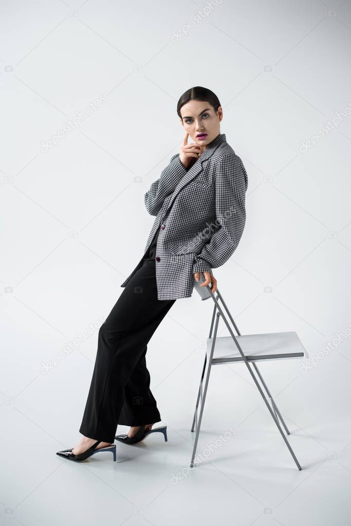 glamour fashionable woman posing in retro suit near chair, on grey 