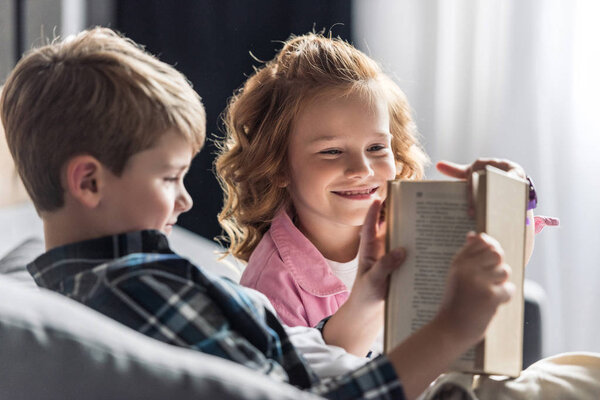 маленький мальчик читает книгу, пока его сестра перебивает его
