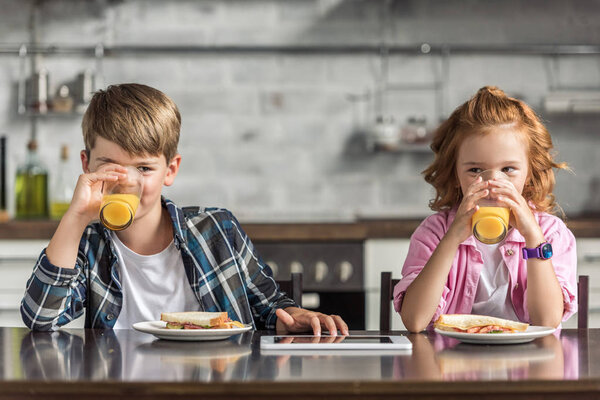 little brother and sister drinking orange juice together during breakfast