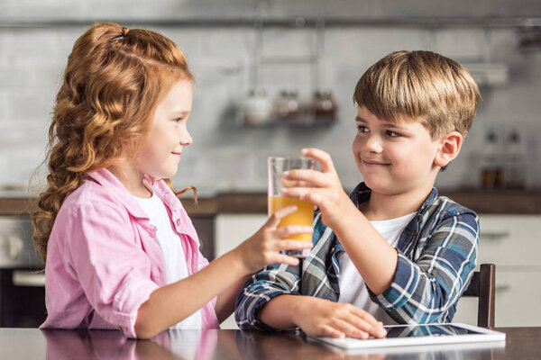 smiling little sister giving glass of orange juice to her brother