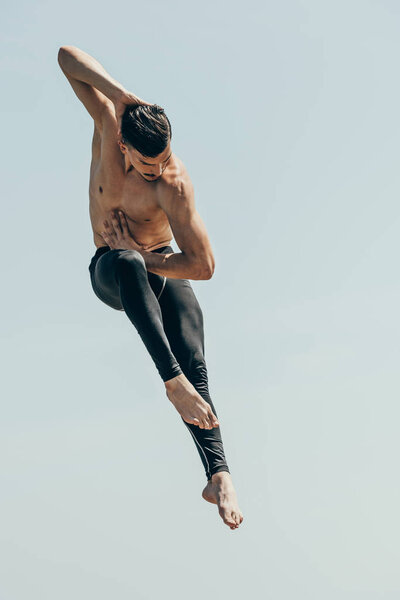 motion shot of handsome shirtless dancer in jump against blue sky