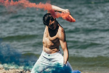 shirtless man dancing with red and blue smoke sticks in front of water surface clipart