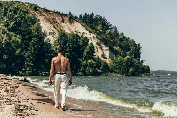 Widok Tyłu Shirtless Człowieka Idącego Przez Piaszczystej Plaży — Zdjęcie stockowe