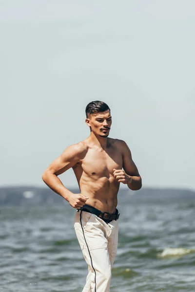 Przystojny Mężczyzna Shirtless Jogging Naprzeciwko Oceanu — Darmowe zdjęcie stockowe