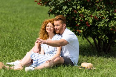 Kızıl saçlı adam el ile kız parkta çim üzerinde gösteren gülümseyen