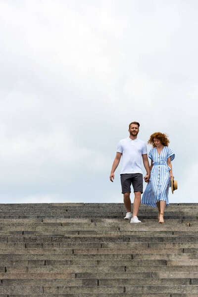 low angle view of redhead couple holding hands and walking on stairs 