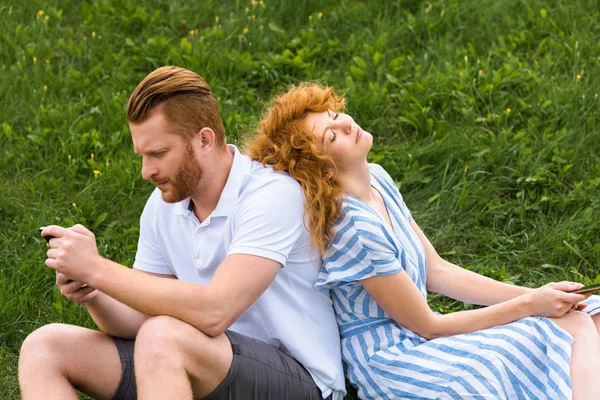 Redhead Couple Smartphones Sitting Back Back Grassy Meadow — Free Stock Photo