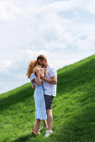 Young Redhead Woman Covering Face Straw Hat While Kissing Boyfriend — Stock Photo, Image