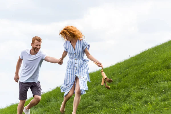 Smiling Redhead Couple Holding Hands Running Grassy Hill — Stock Photo, Image