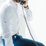 Business man talking on rotary telephone while sitting on table with gun