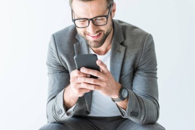 gri elbiseli smartphone, üzerinde beyaz izole kullanarak gülümseyen yakışıklı