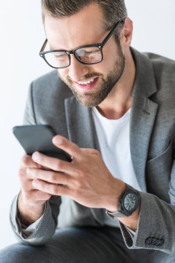 gri ceketli beyaz izole smartphone kullanarak mutlu sakallı adamı