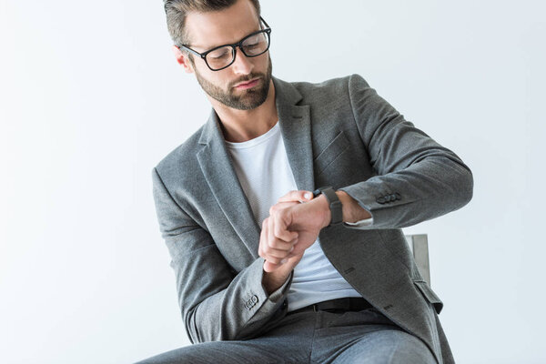 handsome bearded businessman in gray suit looking at watch, isolated on white
