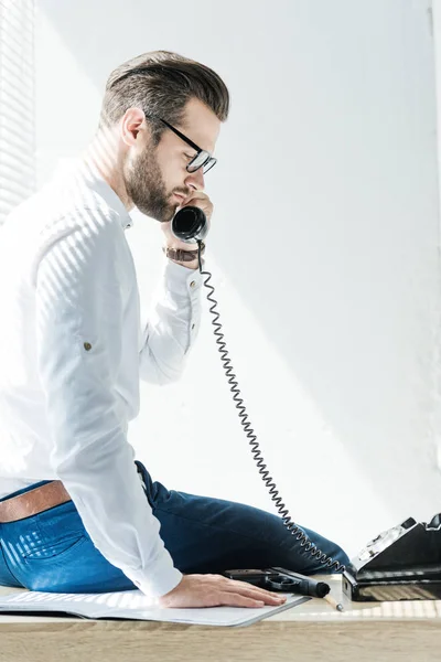 Бородатый Бизнесмен Разговаривает Ротационному Телефону Сидя Столе Пистолетом — Бесплатное стоковое фото
