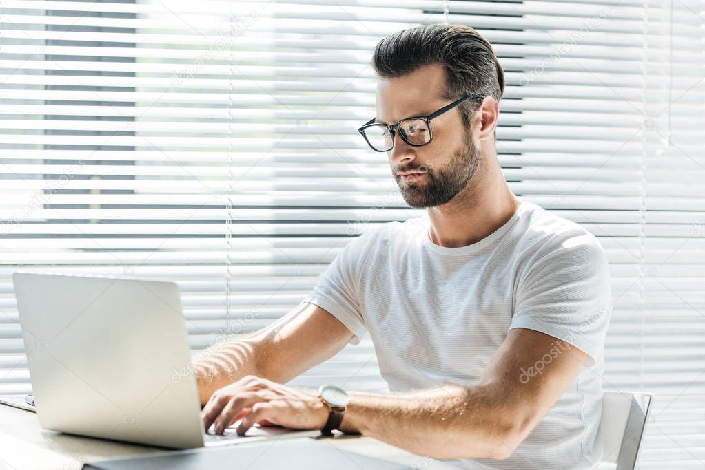 concentrated man in eyeglasses using laptop at workplace
