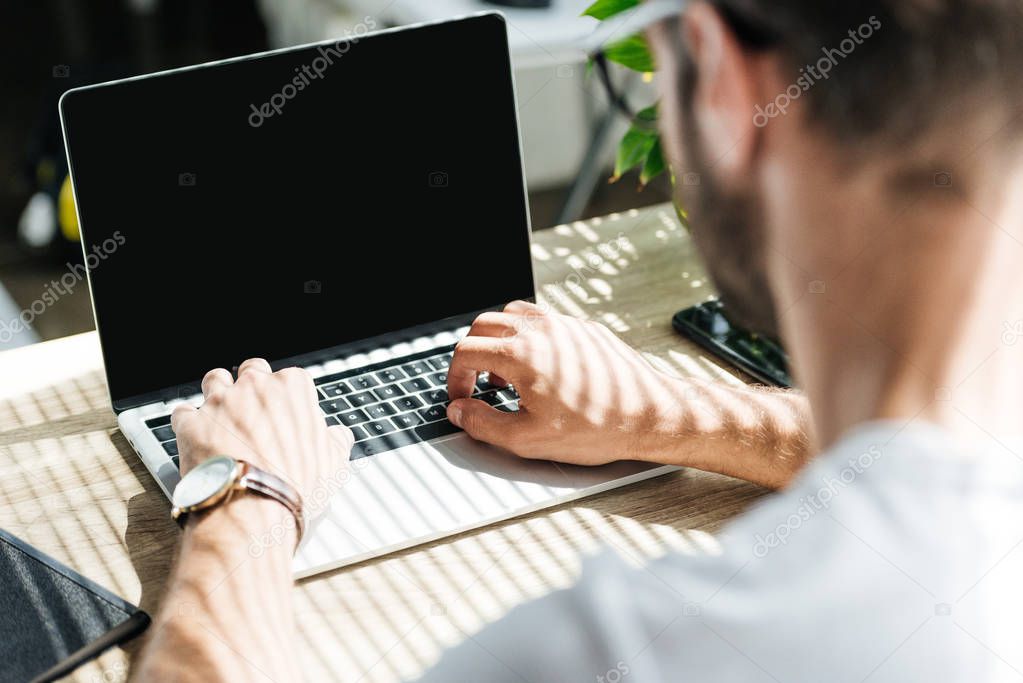 back view of man using laptop with blank screen on workplace