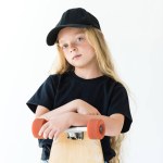 Beautiful child in black cap and t-shirt standing with skateboard and looking at camera isolated on white