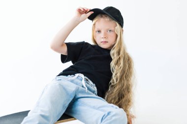 cap ayarlama ve kaykay üzerinde oturan beyaz izole ederken kameraya bakarak uzun kıvırcık saçlı güzel çocuk