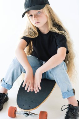 uzun kıvırcık saçlı kaykay üzerinde oturan ve üzerinde beyaz izole kamera bakarak çocuğun yüksek açılı görünüş