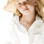 Retrato de niño adorable en sombrero de mimbre sonriendo a la cámara en blanco