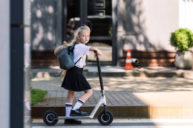 sırt çantası ve scooter sürme ve sokakta kameraya bakarak ayıcık ile sevimli kız öğrenci