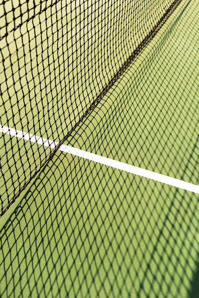 close up view of net with shadow on green tennis court