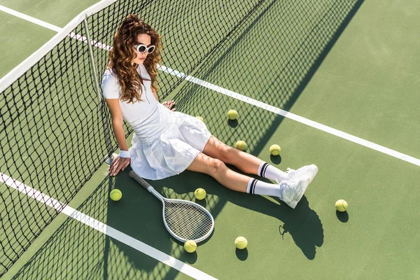 高角度的时尚网球运动员在白色运动服和太阳镜坐在网上网球设备周围网球场 — 图库照片