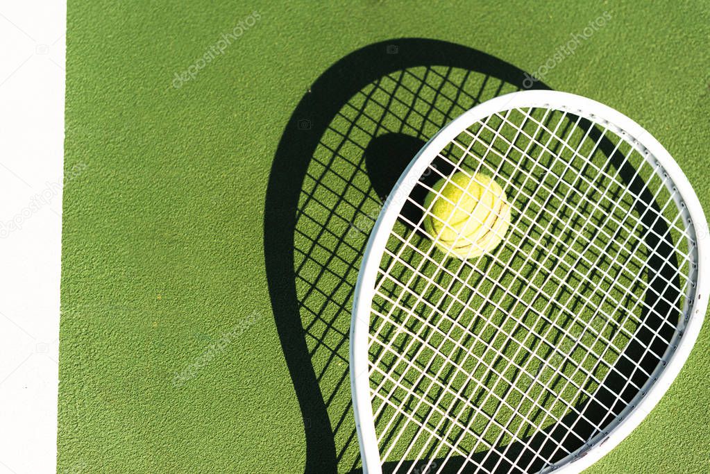 top view of tennis racket and ball lying on green tennis court