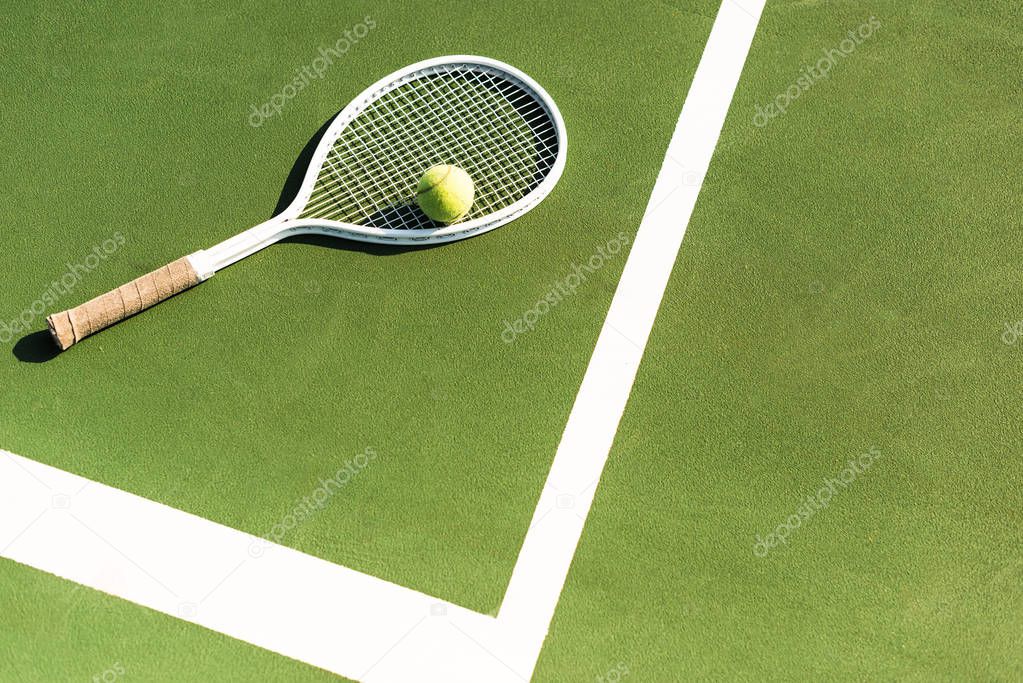 close up view of tennis racket and ball lying on green tennis court