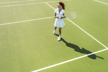 Beyaz tenis kortunda tenis oynamaya Tekdüzen genç çekici kadın yan görünüm