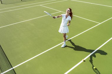 Beyaz tenis kortunda tenis oynamaya Tekdüzen genç çekici kadın yan görünüm