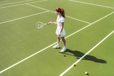 Beyaz tenis kortunda tenis oynamaya Tekdüzen genç çekici kadın yan görünüm