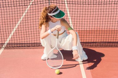Beyaz giyim ve tenis net sahada oturan tenis raketi kapaklı şık kadın