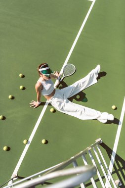 high angle view of beautiful woman in stylish white clothing sitting on tennis court with balls and racket around clipart