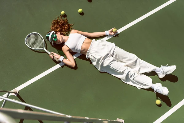 スタイリッシュな女性の白い服とラケット テニス裁判所に横たわっているラケットで横になっているキャップのハイアングル — ストック写真