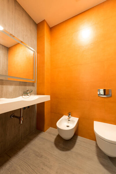 interior of modern bathroom in orange and white colors with toilet and bidet