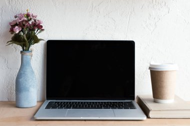 boş ekran, çiçek vazo, kitap ve masada kahve ile dizüstü bilgisayar