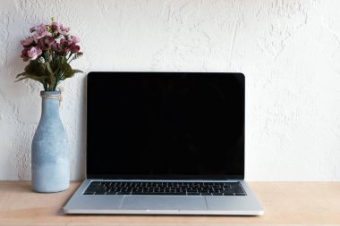 Laptop ile boş bir ekran ve güzel çiçekler vazoda ahşap tablo