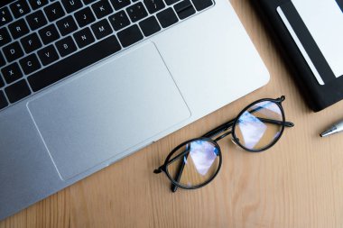 ahşap masa üzerinde laptop, Gözlük, defter, kalem ve kredi kartı üstten görünüm