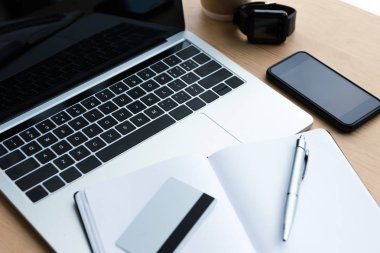 dizüstü bilgisayar, akıllı telefon, smartwatch ve boş defter kalem ve ahşap masa üzerinde kredi kartı ile