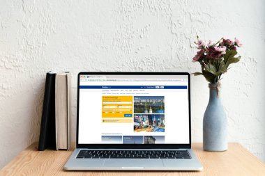 rezervasyon website ekran, kitaplar ve ahşap masa üzerinde Vazoda Çiçekler ile dizüstü bilgisayar