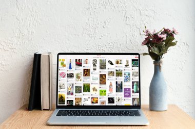 pinterest website ekran, kitaplar ve ahşap masa üzerinde Vazoda Çiçekler ile dizüstü bilgisayar