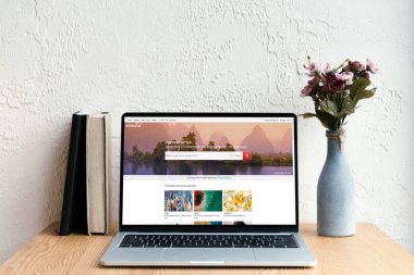 shutterstock website ekran, kitaplar ve ahşap masa üzerinde Vazoda Çiçekler ile dizüstü bilgisayar