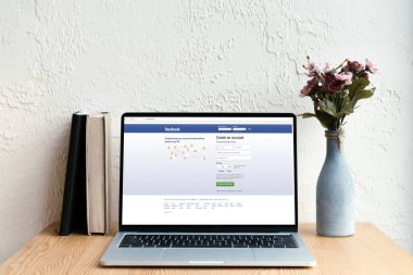 facebook website ekran, kitaplar ve ahşap masa üzerinde Vazoda Çiçekler ile dizüstü bilgisayar