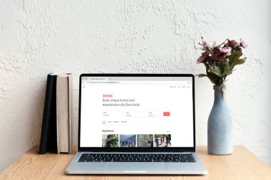 airbnb website ekran, kitaplar ve ahşap masa üzerinde Vazoda Çiçekler ile dizüstü bilgisayar