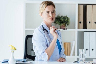 çekici kadın doktor stetoskop Office masada gözlük tutan boyun üzerinden ile beyaz ceket 