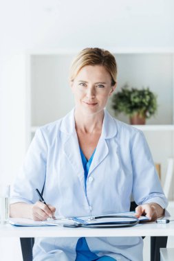 Yetişkin kadın doktor masada office panosu yazılı beyaz ceket 