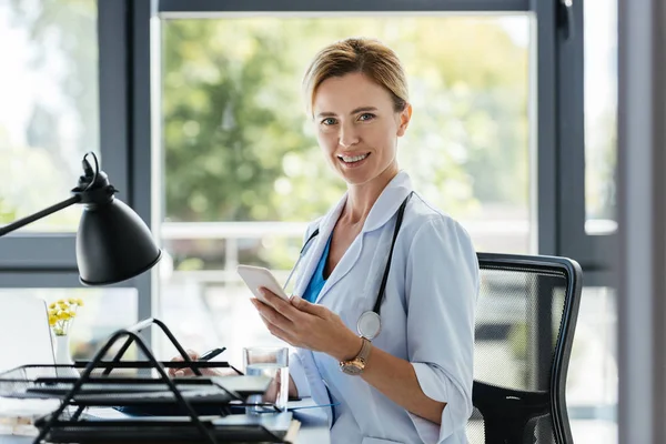 Beautiful Female Doctor Smartphone Hand Looking Camera Sitting Table Office — Stock Photo, Image