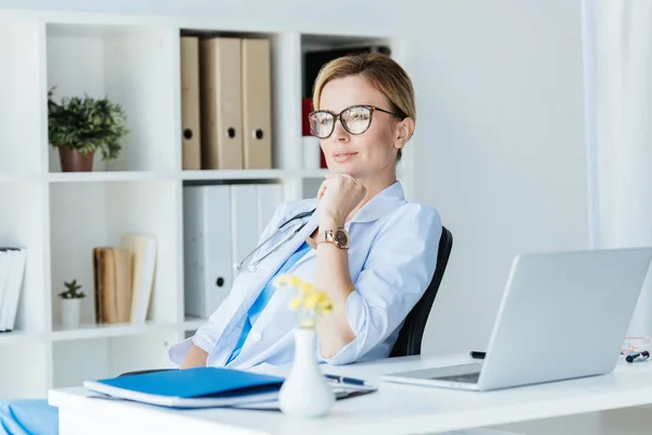Pensive Adult Female Doctor Eyeglasses Sitting Table Laptop Office — Stock Photo, Image