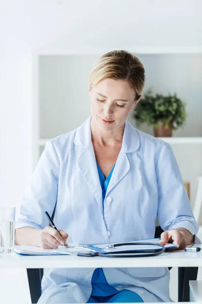 Vrouwelijke Arts Witte Jas Aan Tafel Office Klembord Schriftelijk Gericht — Stockfoto